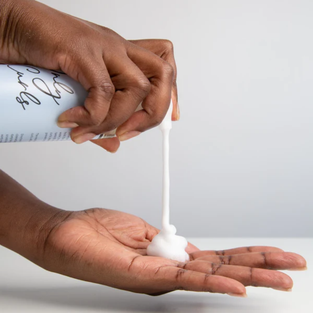 Iemand drukt op de dispenser van de Only Curls Volumising Curl Mousse. De mousse valt in de ander hand van de gebruiker als sfeerfoto om de substantie te laten zien.