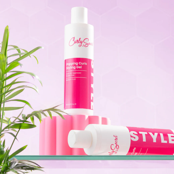 Twee Popping Curls Gel van Curly Secret in een sfeeromgeving met een plant, en roze/paars achtergrond.