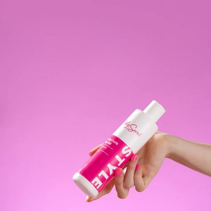 Popping Curls Styling Gel in hand met roze nagellak dat match bij de achtergrond en kleur van de popping curls gel van Curly Secret