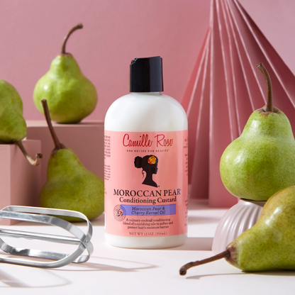 Camille Rose Moroccan Pear Conditioning Custard in sfeeromgeving met echte peren op de achtergrond en met een roze studioachtergrond