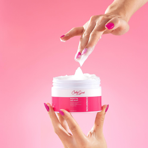 Iemand die die substantie laat zien van de Curly Secret Repairing Hair Mask door het eruit te halen.